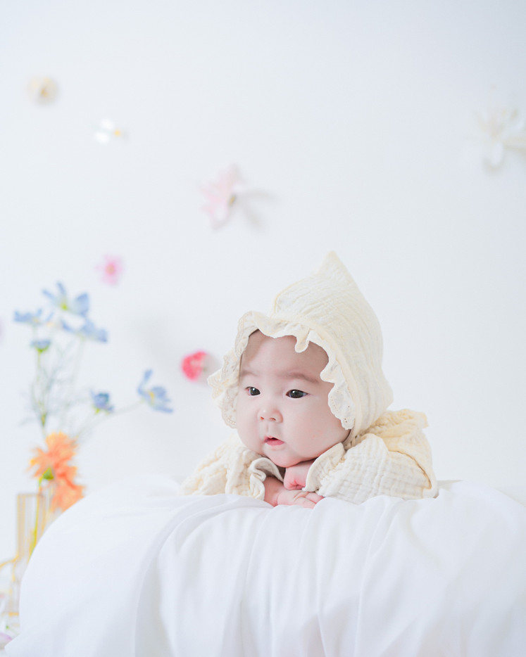 작은 왕관을 쓰고 흰 침구에 누운 아기의 50일 사진